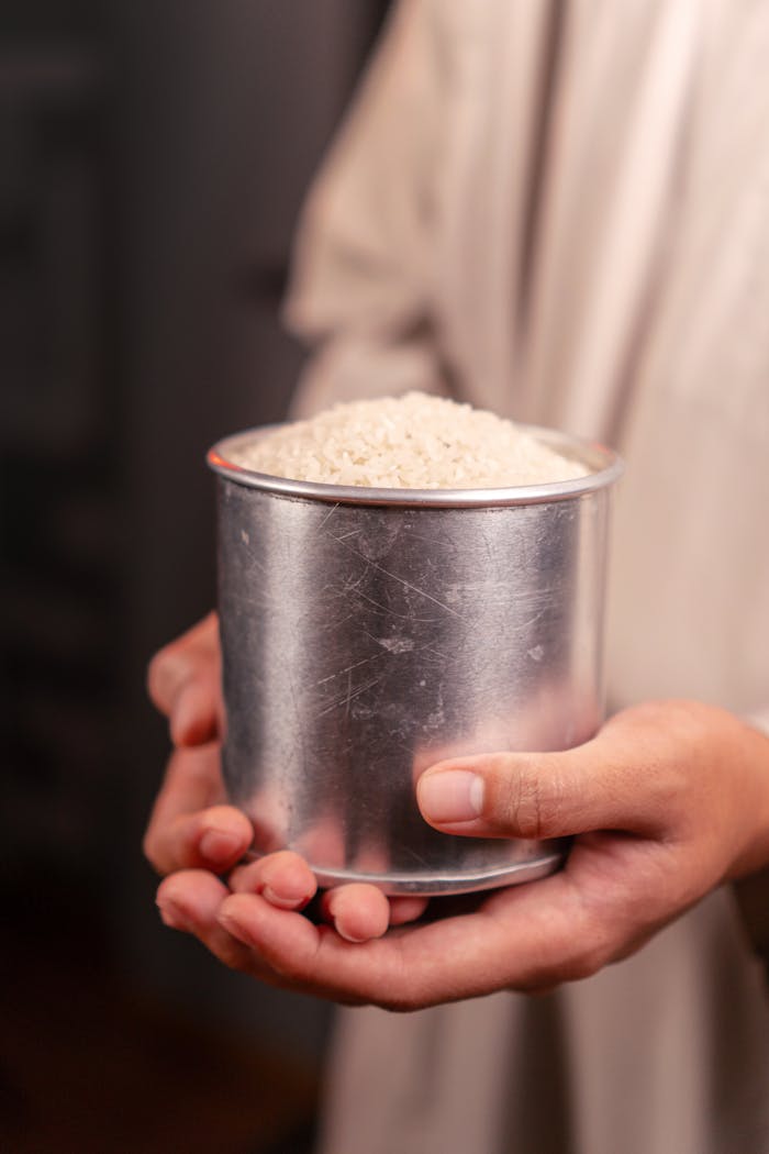 who-we-are Close-up of hands holding a tin cup full of uncooked white rice, symbolizing abundance.